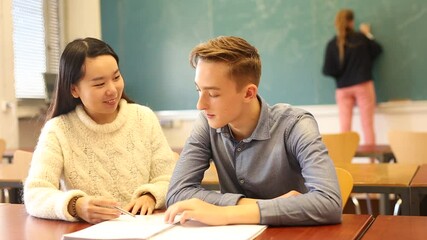Two teenage students Chinese girl and European guy studying together in schoolroom. Education concept