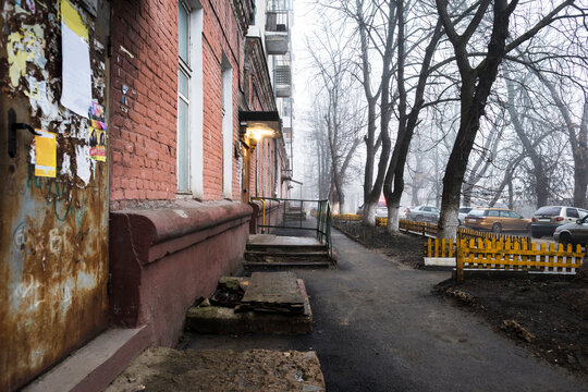 Courtyard of a brick five-storey apartment building, torn off advertisements on the walls, parked cars.