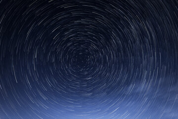 Obraz premium Stellar trails, the rotation of bright stars at night around the Polar Star against a blue sky