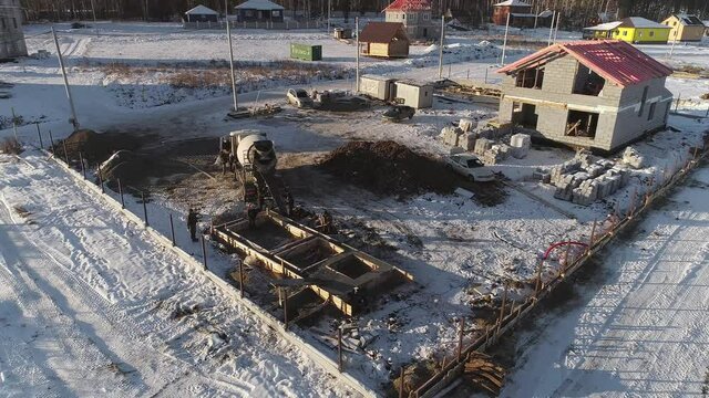 Aerial view of Construction site in a cottage village. A concrete mixer truck unloads concrete into the foundation frame of the future house. Workers Pouring Concrete From Truck. A house and a fence a