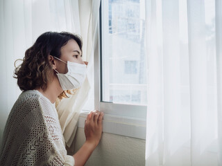 Beautiful lonely Asian woman wearing medical face mask looking out the window.