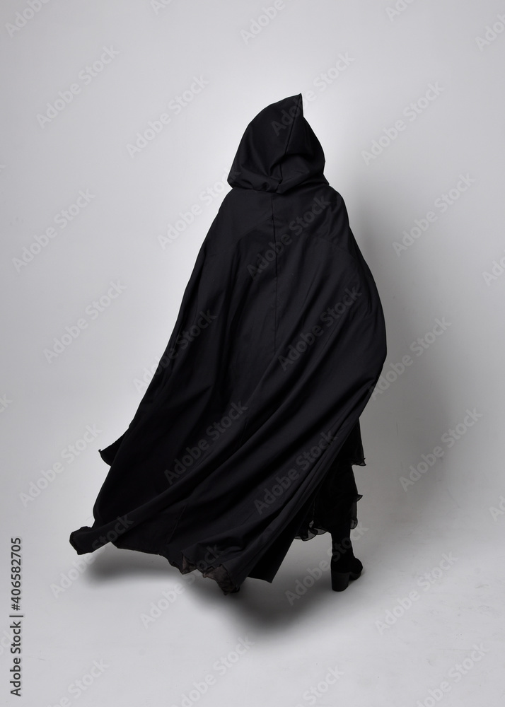 Wall mural Full length portrait of pretty black haired woman wearing long dark gown nada cloak.  Standing pose facing away from the camera, against a  studio background.