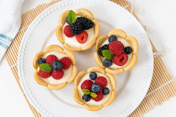 Delicious pastry mini fruit cream cheese pies or tart cakes with fresh raspberry, blueberry and blackberry