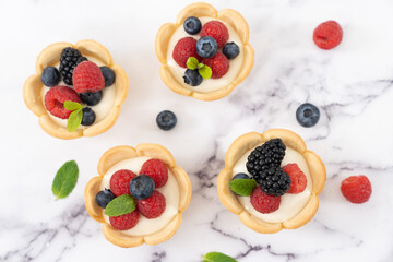 Delicious pastry mini fruit cream cheese pies or tart cakes with fresh raspberry, blueberry and blackberry