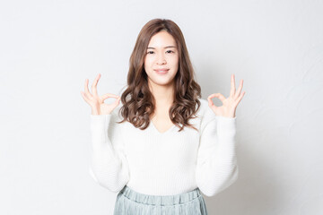 白い壁の前に立ってOKのジェスチャーをする若い女性