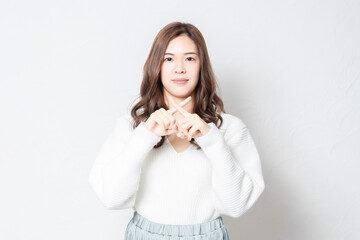 白い壁の前に立ってNGのジェスチャーをする若い女性