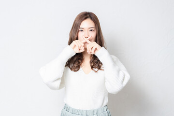 白い壁の前に立ってNGのジェスチャーをする若い女性