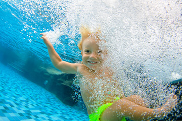 Funny portrait of child learning swimming, dive in blue pool with fun - jumping deep down...