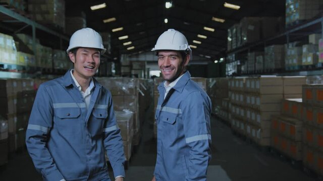 portrait of asian male and caucasian male professional enginner wearing uniform hardhat standing and smile with confident and cheerful in warehouse factory