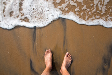 Top view of feet in the wet sand by the sea shore with the waves approaching.