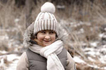 Cute teenage girl in a warm hat and scarf on the background of a campfire in the autumn forest. Winter fashion clothes