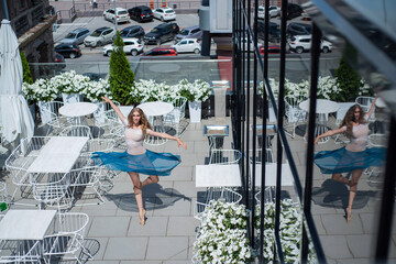 Graceful ballerina dancing outdoors on a warm summer day. Young flexible woman in pointe shoes and ballet tutu posing in a street cafe