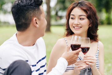 Beautiful smiling young woman drinking red wine at romantic date with her boyfriend in park on Valentines day