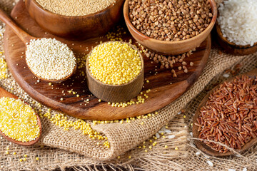 White and red rice, buckwheat, amaranth seeds, corn groats, quinoa and millet in bowls on a brown wooden table. Gluten-free cereals. Closeup