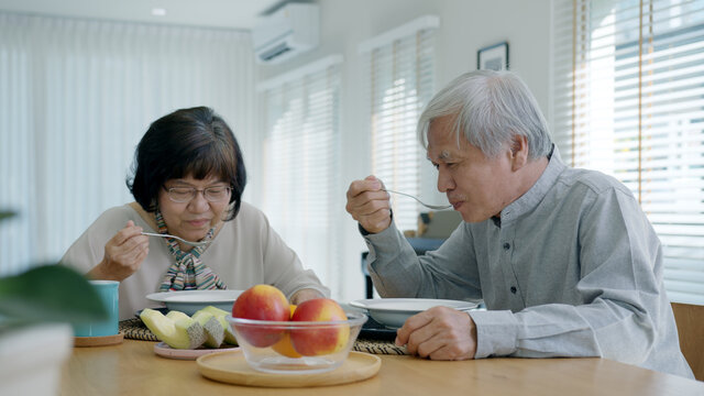 Attractive Young Senior Asian Citizen Couple Happy Sit And Talk, Eat Soup For Healthy Nutrition Breakfast Meal On Dining Table At Home In Morning In Routine Lifestyle In Old Asian People Concept.