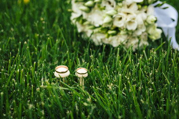Beautiful wedding rings lie on wooden surface against background of bouquet of flowers. Declaration of love, spring. Wedding card, Valentine's Day greeting. Wedding rings. Wedding day details