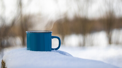 Winter coffee in a blue cup on the snow in the forest. Winter atmospheric background with coffee in nature. Sunny frosty morning.