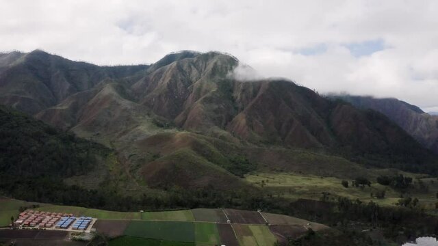 Aerial panoramic view of mountains near Constanza in Dominican Republic cloudy sky and plowed green land on the valley close to the rocky mountains peak