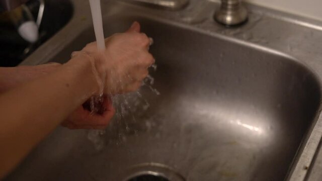 Feminine hands washing away dirt and germs in the kitchen sink - slow motion isolated - 2020 global pandemic