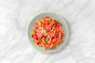 Penne pasta with chicken, tomato sauce and parsley, overhead shot on a white marble background