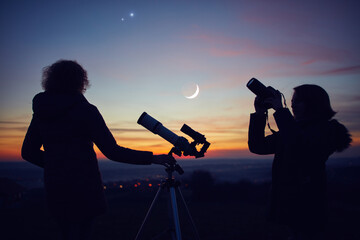 Mother and daughter observing stars, planets, Moon and night sky with astronomical telescope.