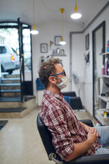 Man with surgical medical mask sitting in a hair salon.