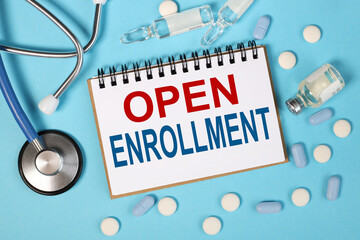open enrollment, text on white notepad paper on blue background near stethoscope, tablets, ampoules