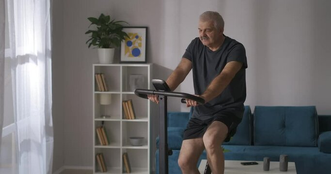 elderly athletic man is training on exercise bike at home, portrait shot, keeping physical condition