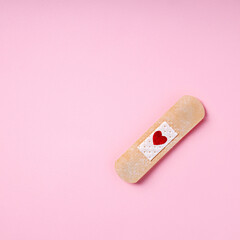 Love layout made with first aid plaster with heart shaped stain on pastel pink background. Minimal broken heart, romantic suffering or valentines concept. Flat lay, greeting card.