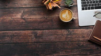 Top view of hipster vintage workspace with laptop, stationery notebooks and a cup of coffee on wooden table. Copy space for advertise text.