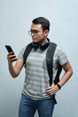 portrait of student, young man looking at cellphone with earphones and backpack on a white background