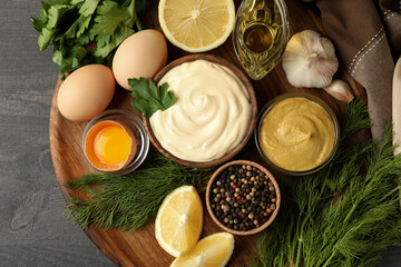 Board with bowl of mayonnaise and ingredients for cooking on dark wooden background