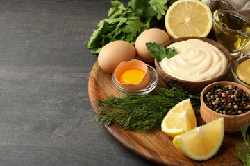 Board with bowl of mayonnaise and ingredients for cooking on dark wooden background