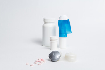 Contact lenses container and pile of pills placed against bottles with medicines and eye drops on white background in studio 