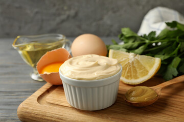 Board with bowl of mayonnaise and ingredients for cooking on wooden background