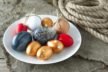 Trendy colored easter eggs, canvas and rope and feathers on a plate on wooden table. Preparation for easter holidays. Fesstive composition.