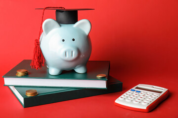 Piggy bank with graduation hat, books, calculator and coins on color background