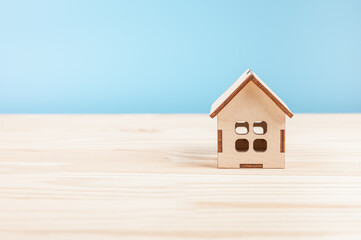Obraz na płótnie Canvas small wooden model house on wood table. Mini residential craft house on blue background. Close-up view of small house model on wooden table on blue, insurance Mortgage concept