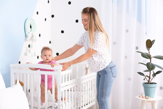 Mother With Cute Baby Standing In Crib At Home