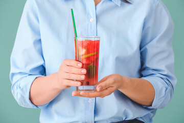 Woman holding glass of cold watermelon lemonade on color background