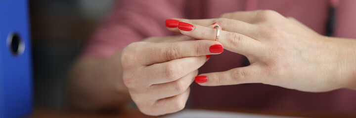 Woman taking off her wedding ring from her finger in front of documents close-up. Divorce and division of property concept