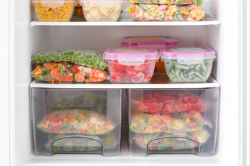 Containers and plastic bags with frozen vegetables in refrigerator