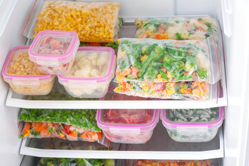 Containers and plastic bags with frozen vegetables in refrigerator