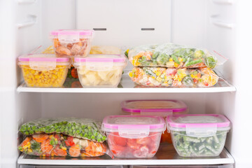 Containers and plastic bags with frozen vegetables in refrigerator