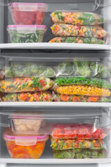 Containers and plastic bags with frozen vegetables in refrigerator