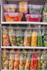 Containers and plastic bags with frozen vegetables in refrigerator, closeup