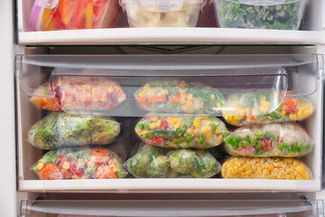 Plastic bags and containers with frozen vegetables in refrigerator