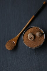 Nutmeg.Whole and grated nutmeg in a  black cup and wooden spoon on a black slate background.Spices and herbs concept. Dark mood.Whole and partly grated nutmeg seeds 