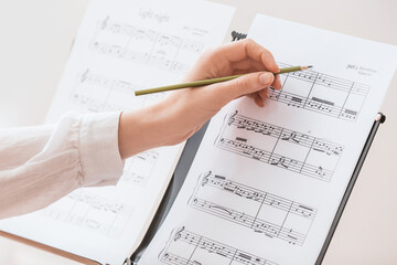Female hand and note stand with music sheets on light background