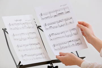 Female hands and note stand with music sheets on light background